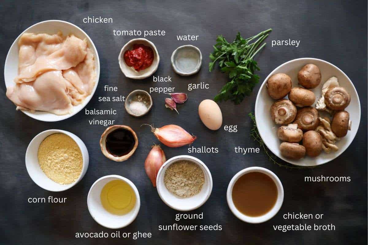 All ingredients for chicken jaegerschnitzel with mushroom sauce are displayed on a dark grey surface and labeled