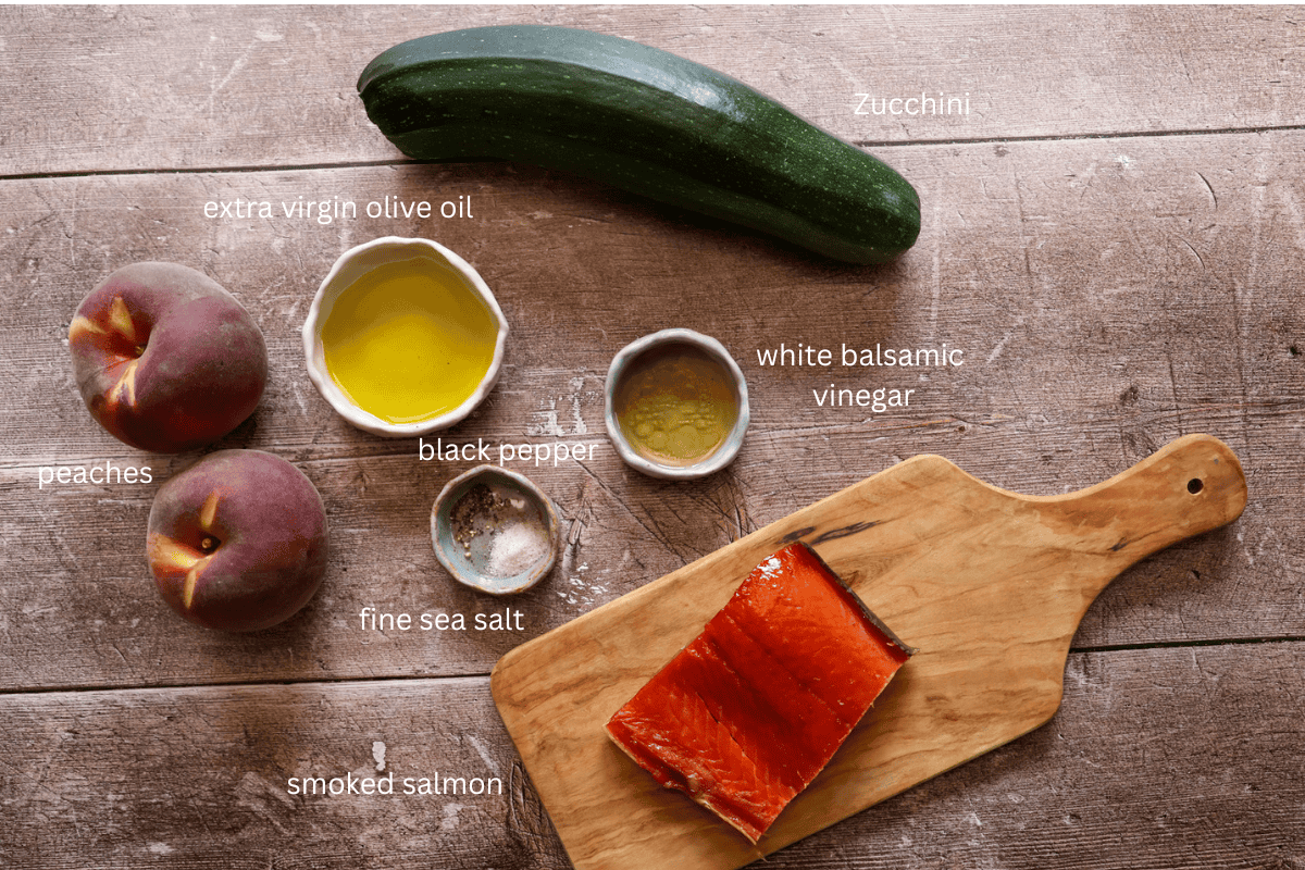 All ingredients for smoked salmon, peach, and zucchini salad are displayed and labeled on a wooden surface