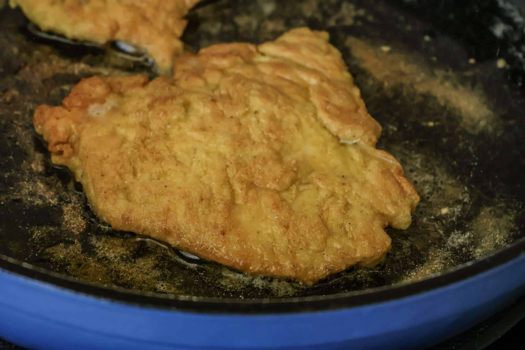 Schnitzel cooking in a blue enameled cast iron pan