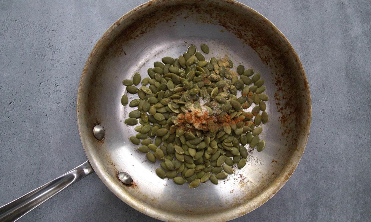 pumpkin seeds in a pan along with spices ready to be cooked